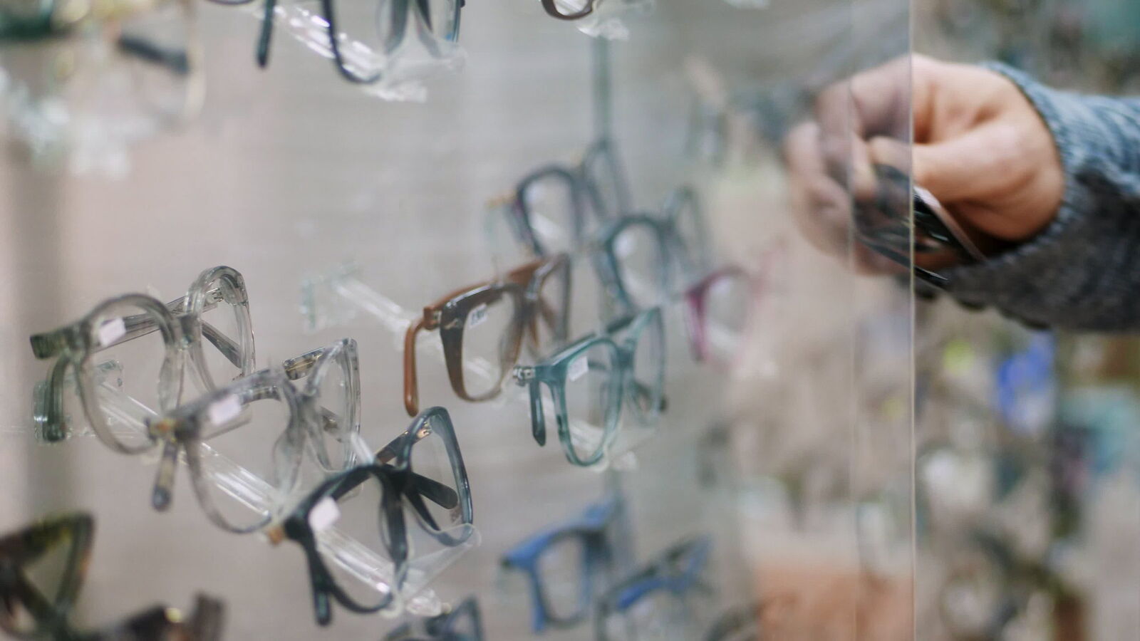 Fassungen in einer Wandauslage im Optikgeschäft, eine Hand greift nach einer Brille